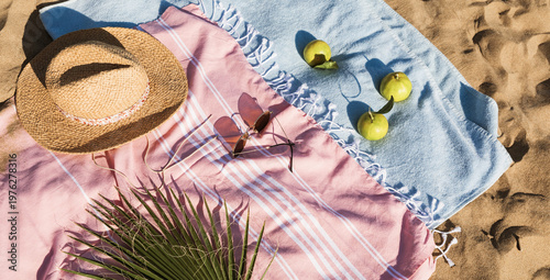 Summer beach accessories flat lay on sand background. Holiday travel, tropical concept. Straw hat, sunglasses, towel and fruits. Sun shadow and sunlight