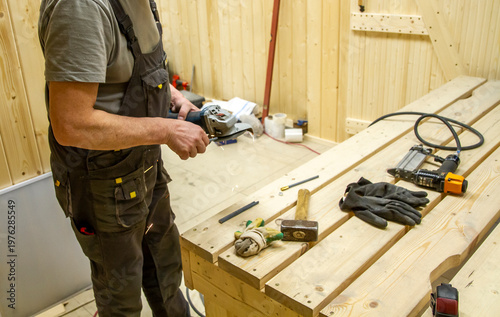 The image depicts a woodworking scene with a person holding a handheld power tool, likely a grinder or saw, near a custom-built wooden workbench. Craft