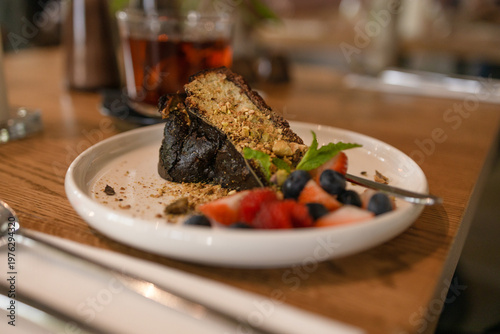 Slice of chocolate cake served with fresh berries and tea on wooden table in cozy cafe environment with soft natural light. High quality photo
