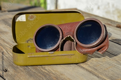 Professional retro safety glasses for gas welding in a metal box container, dark protective eyewear on a wooden surface.