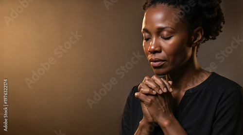 Black woman praying with eyes closed and clasped hands. Religious faith and spirituality concept. Studio portrait with copy space on dark background