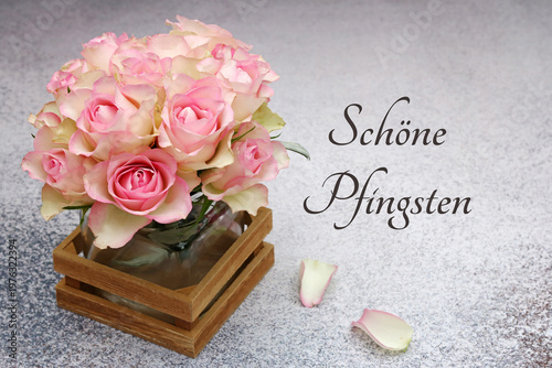 Elegante Pfingstgrüße: Vase mit rosa Rosen in einem  auf grauem Untergrund mit zwei Rosenblättern und dem Schriftzug 'Schöne Pfingsten'