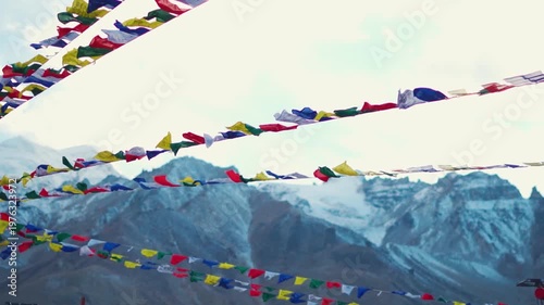 Landscape shot of colorful Buddhist prayer flags waving in front of snow covered Himalayan mountain peak during the winter season as seen from Padum town in Zanskar Valley in remote Ladakh, India.