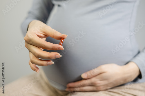 Close-up of a pregnant woman holding a brown capsule pill, concept of prenatal supplements, medication, and maternity healthcare.