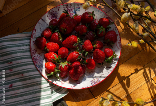 Fotografija Fresh strawberries arranged in a floral ceramic bowl on wooden floor near willow catkins