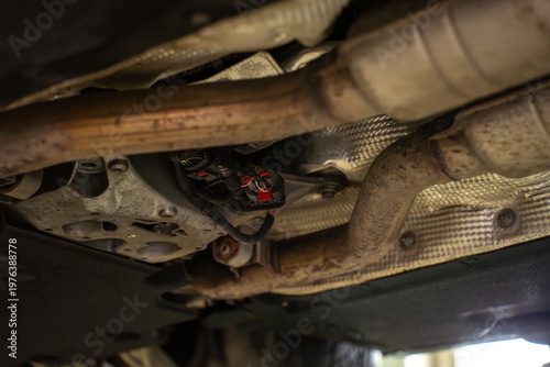 Underside view of car exhaust system with catalytic converters and pipes, showing emission control components installed along vehicle chassis.