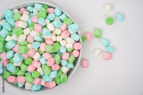 A light gray bowl overflows with various pastel mini marshmallows, including white, pink, green, and blue