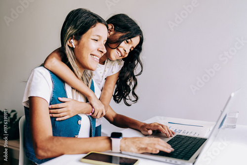 Happy Asian mother working at home with her daughter hugging her - Smart working and family concept