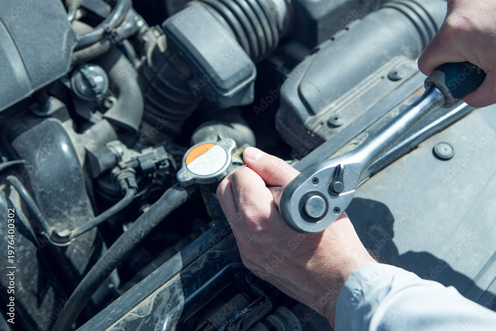 Fototapeta premium Auto mechanic using a wrench to check the oil level of the car