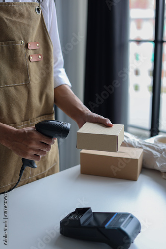 A person using a barcode scanner to scan a small cardboard box in a retail shop for inventory management or preparing an order for shipping.