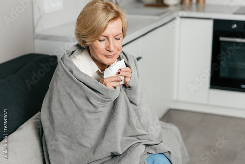 Tableau sur toile Elderly woman feeling unwell wrapped in blanket holding tissue