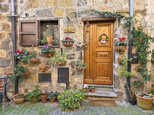 Traditional stone house entrance in the medieval village of Bolsena decorated with colorful flowers, hanging plants and a wooden door, Lazio, Italy