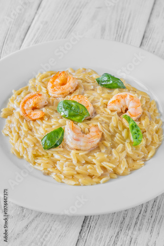 Creamy orzotto pasta topped with grilled prawns and fresh basil on rustic wooden table