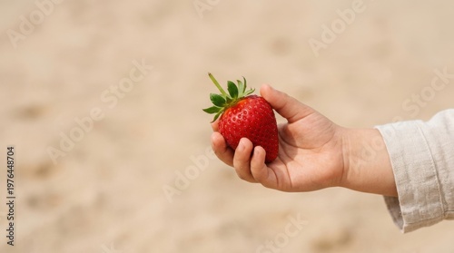 a striking commercial composition of a childs hand holding a vibrant red strawberry against a clean, sandy beige background, highlighting the freshness of the fruit. the