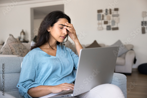 Tableau sur toile Woman sits on sofa at home, experiencing stress, overwhelmed by tasks or remote