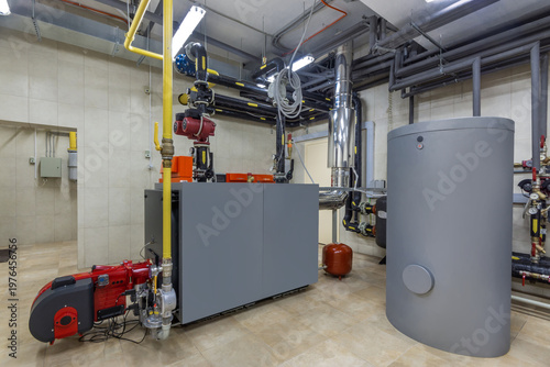 An industrial heating system inside a commercial building. There are pipes, a large tank, and machinery arranged in an organized manner. The equipment is functioning and well-maintained