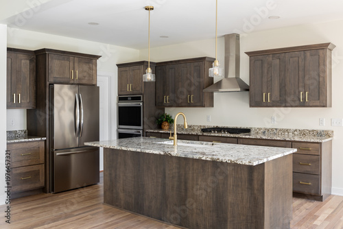 A kitchen detail with a gold faucet on a granite countertop, dark wood cabinets, stainless steel appliances, and gold pendant lights hanging above the island. No brands or labels.