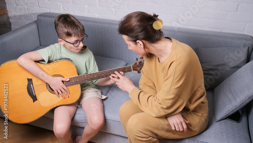 Obraz na plátně Daughter teaching son how to play the acoustic guitar, guiding his fingers on th