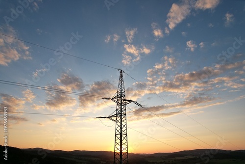 High voltage transmission tower in green landscape during sunset aerial panorama of energy infrastructure