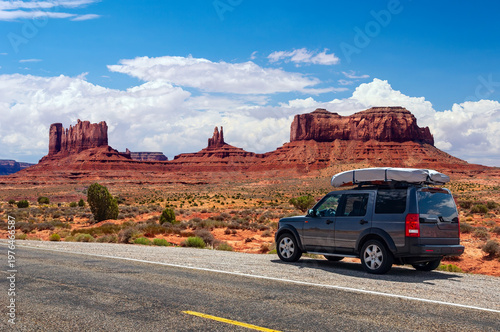 SUV parked along scenic road in Monument Valley with red rock formations under blue sky, American Southwest road trip concept