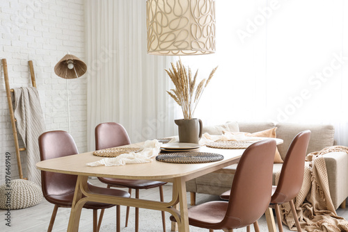 Vase with spikelets and plates on dining table in room