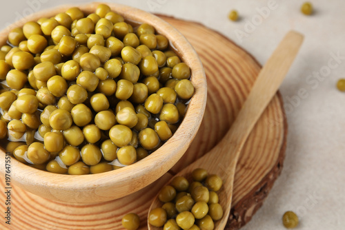 Wooden bowl and spoon with canned green peas on white background, closeup