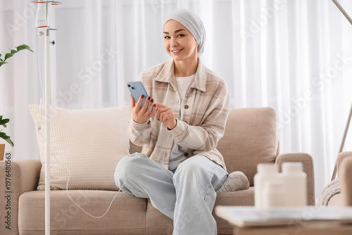 Young woman after chemotherapy using mobile phone on sofa at home. Brain canc...