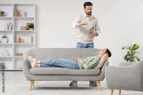 Male psychologist with pendulum hypnotizing young woman on sofa in office