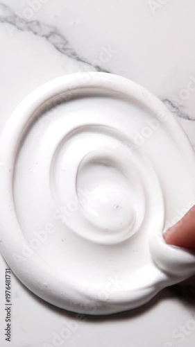 Finger swirling through thick white cosmetic cream or slime on a marble surface, satisfying tactile texture, skincare product testing, smooth consistency and gooey material, macro detail.