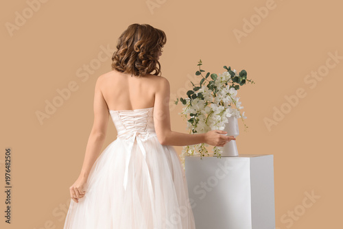 Beautiful bride in wedding dress with flowers on beige background, back view