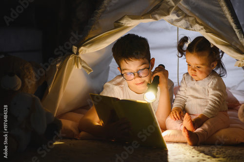 Obraz na płótnie Children reading book with flashlight in blanket fort