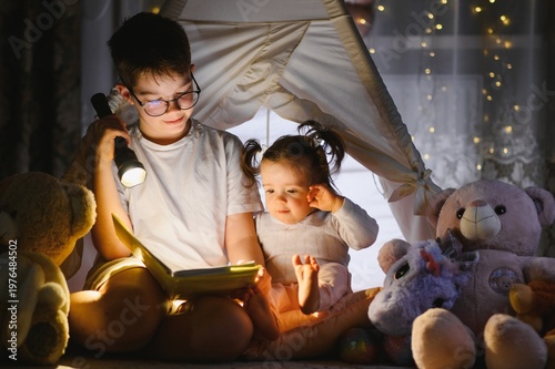 Bild auf Leinwand Siblings reading bedtime story under a tent