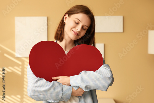 Fotografie Beautiful young happy woman hugging paper heart at home