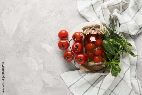 Jar of canned tomatoes with basil, dill and napkin on white grunge background