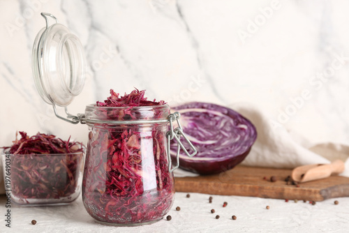 Bowl and jar of tasty red sauerkraut with peppercorns on light background