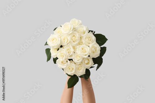 Hands with bouquet of beautiful white roses on light background