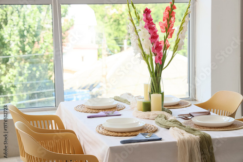 Elegant table setting with plates, candles and beautiful gladiolus flowers