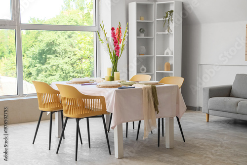 Served dining table with plates and beautiful gladiolus flowers in interior of stylish living room