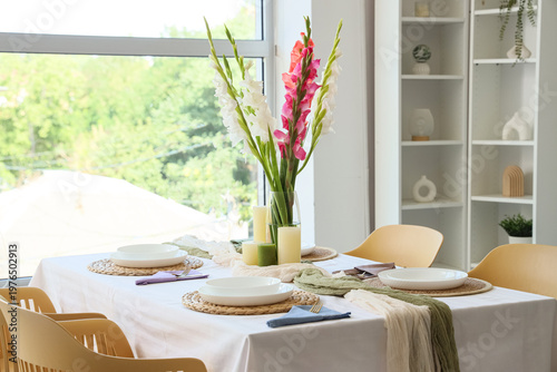 Elegant table setting with plates, candles and beautiful gladiolus flowers