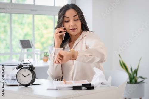 Businesswoman talking by mobile phone and looking at wristwatch in office. Ti...
