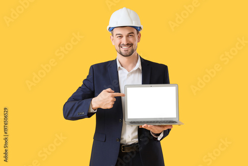 Male architect pointing at blank laptop on yellow background