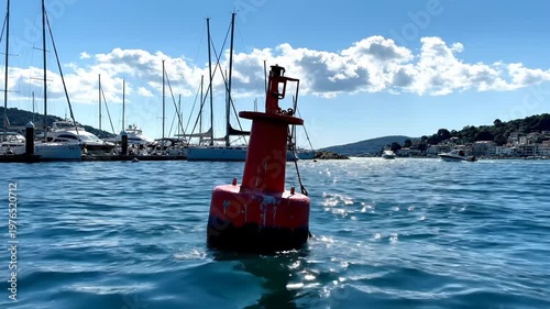 Red nautical navigational buoy floating in a coastal marina with sailboats