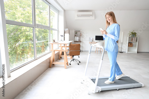 Female doctor with mobile phone training on treadmill in clinic