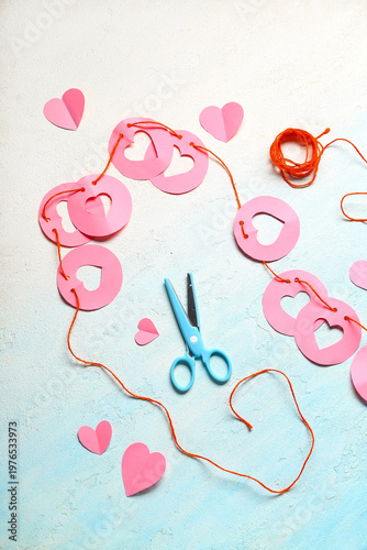 Garland made of pink paper flags with hearts and scissors on blue background. Valentine's Day celebration