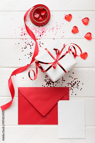 Envelope with blank card, gift box and decor on white wooden background. Valentine's Day celebration