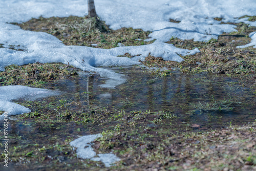 Fotografi Patchy snow and spring melt water pooling across open field, shallow rivulets co