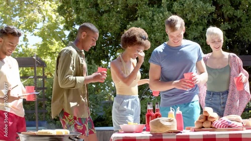 Five friends grilling passing cups at table for barbecue PARTY TIME text appearing obscuring scene