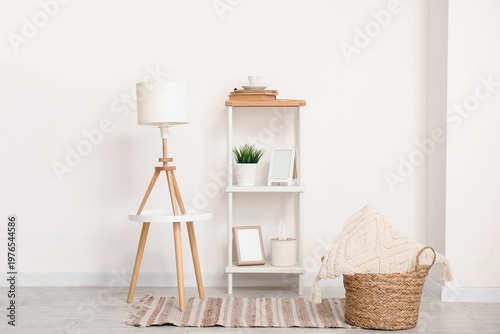Lamp on small table and shelving unit with decor near white wall