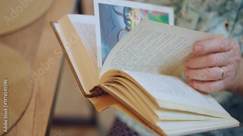 Open book with illustration pages, grandma gently revealing colorful picture while reading aloud, hands showing steady thumb and ring, storytime vibe in sunlit kitchen, turning pages to childlike art,