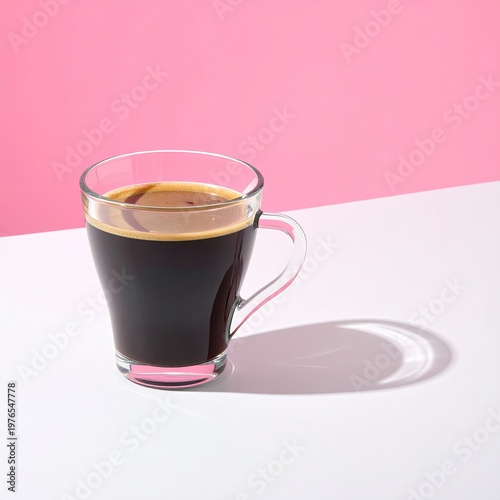Clear glass mug filled with dark coffee, set against pink and white
